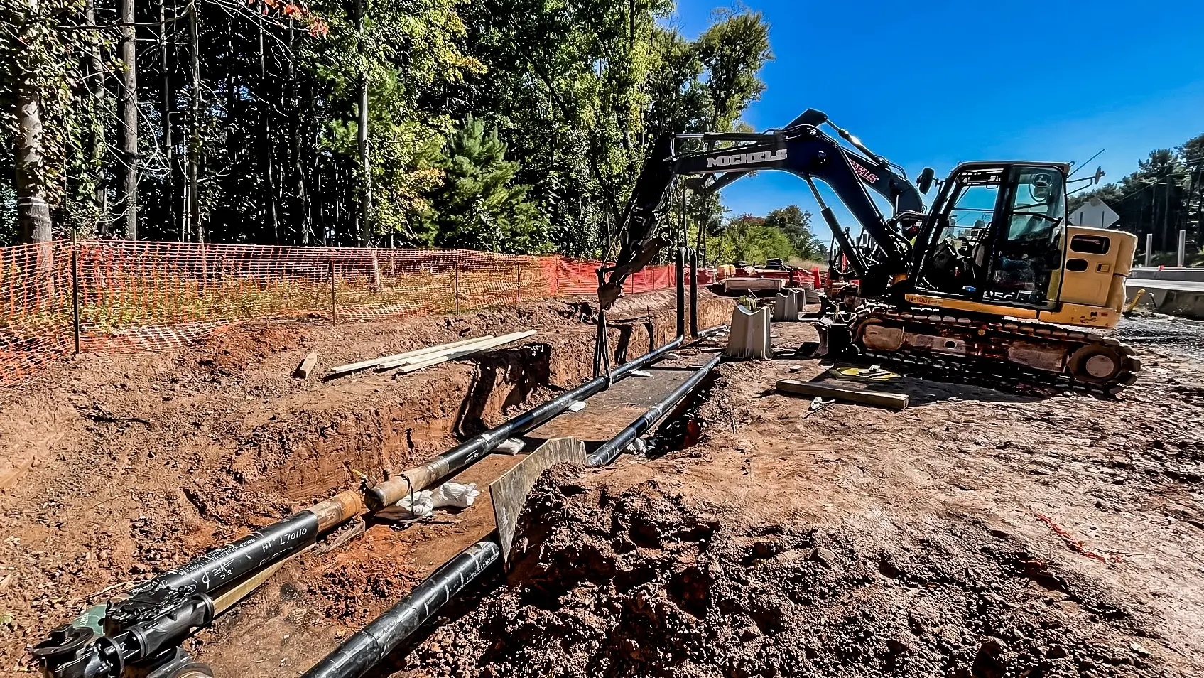 Small excavators perform line lowering of a pipeline into a trench.