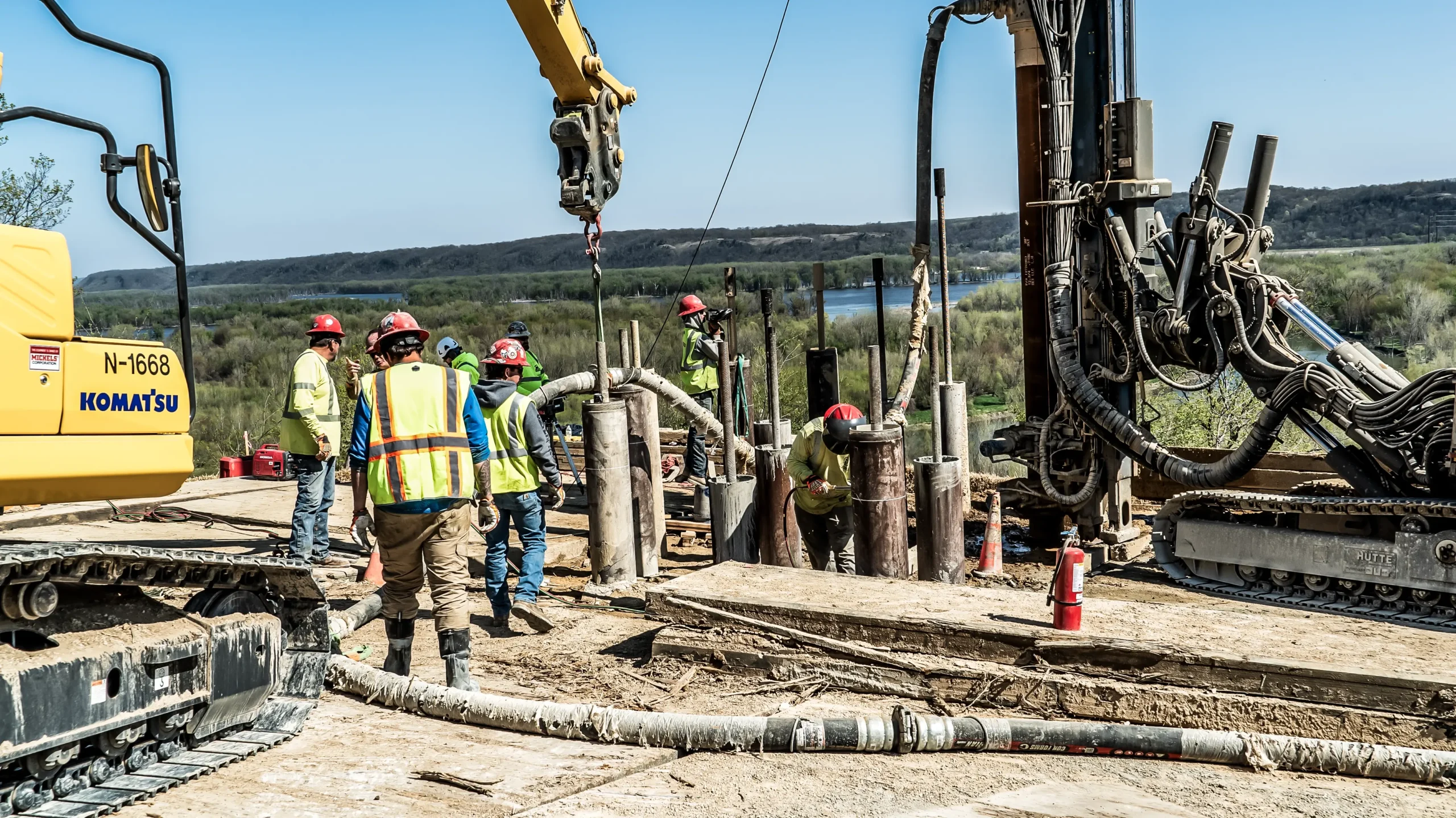 Power foundation shafts are installed by multiple crew members and equipment on a hillside.