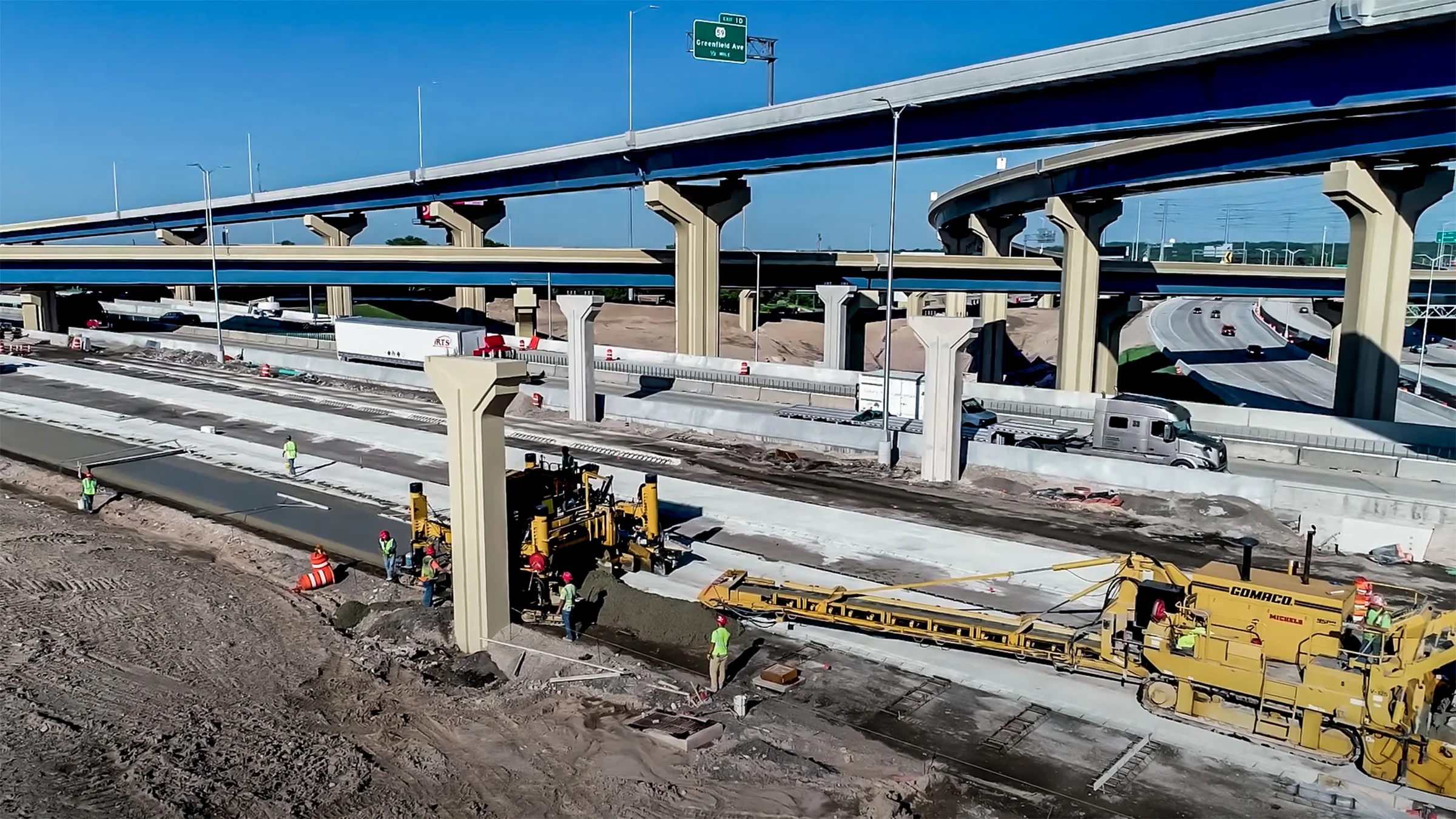 Crew working on paving under a multi-level highway system.