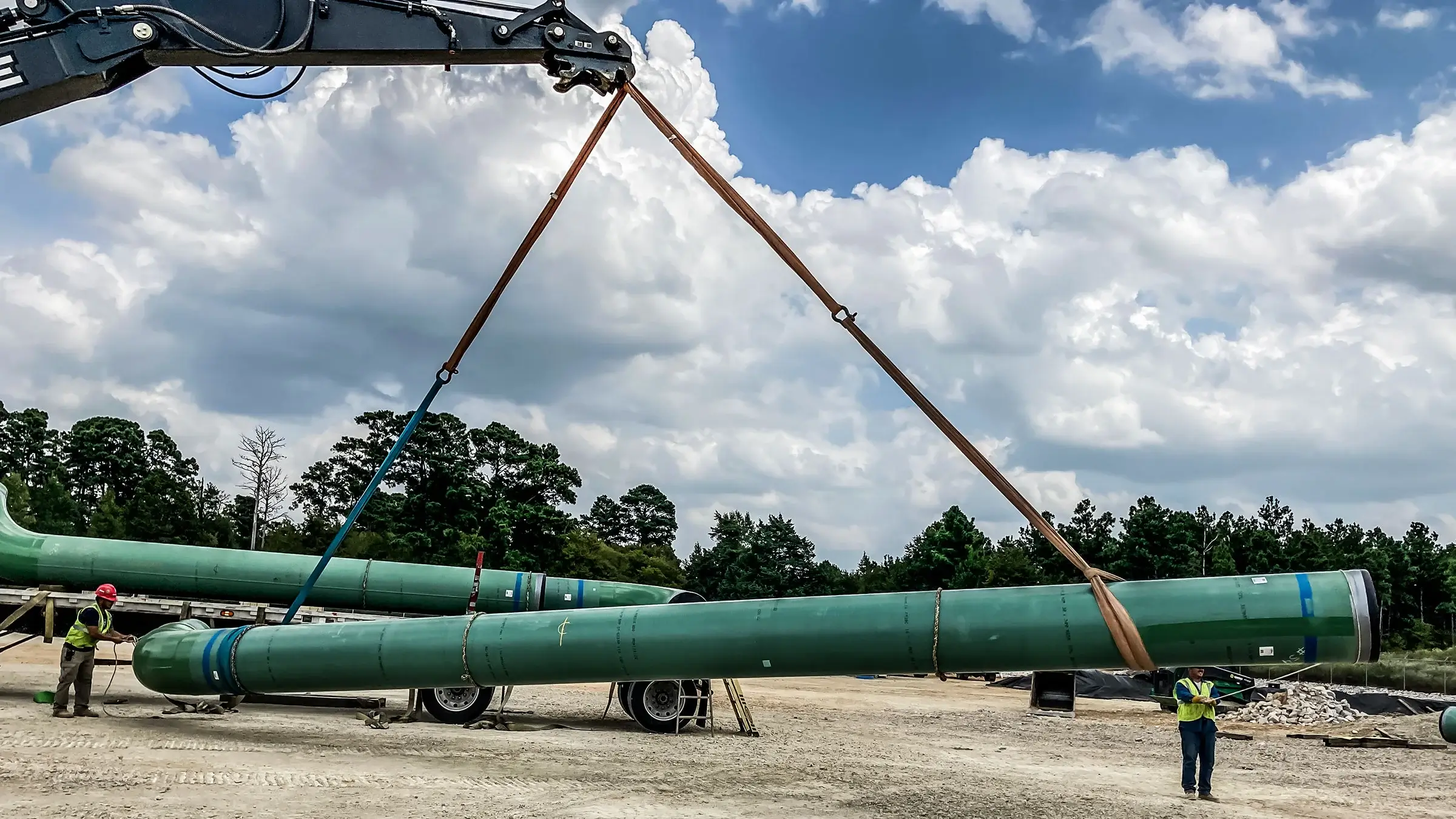 A large portion of large diameter pipe being lifted in the air by heavy equipment