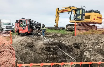 A small HDD rig and trackhoe operate on a dig site