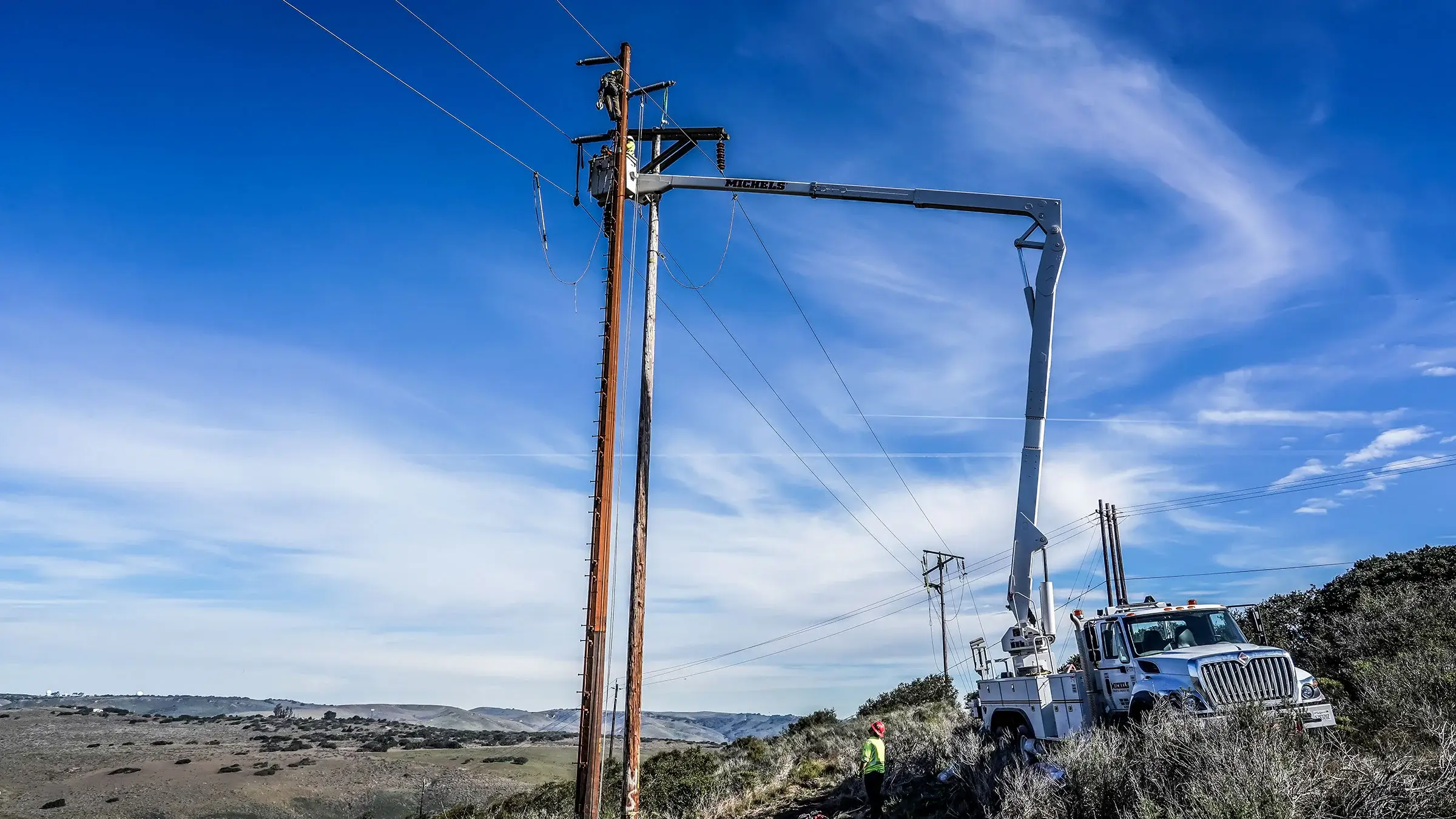 A bucket truck operates on a rural hillside transmission line.