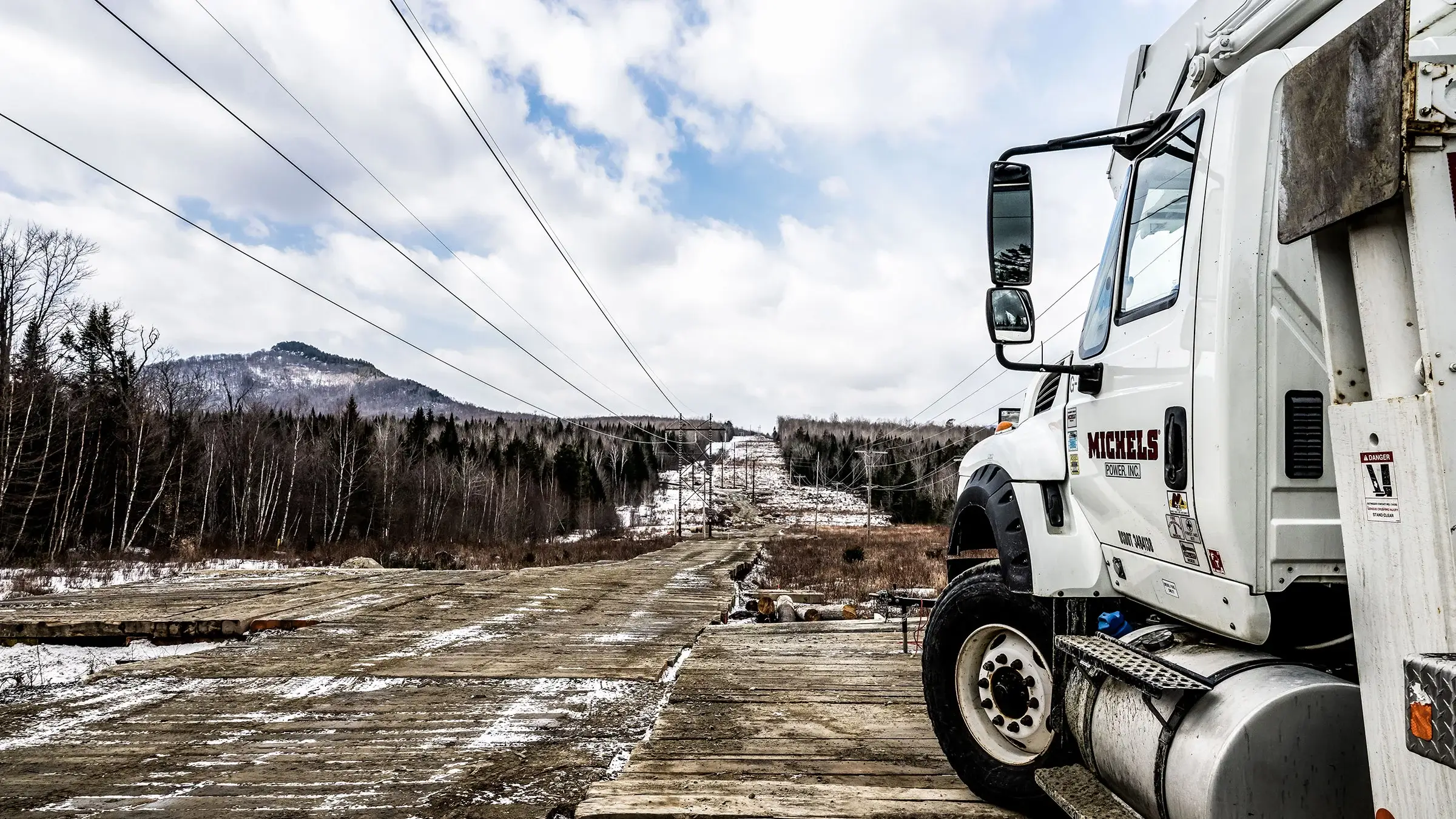 A Michels Power truck parked on matting near a stretch of power lines in the forest