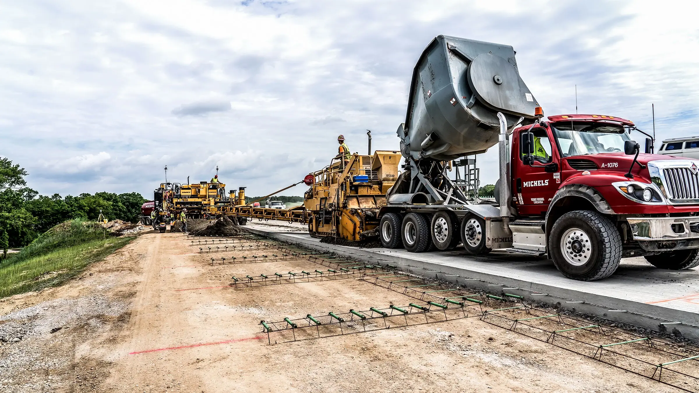 A paving crew lays down concrete from a concrete mixer truck.