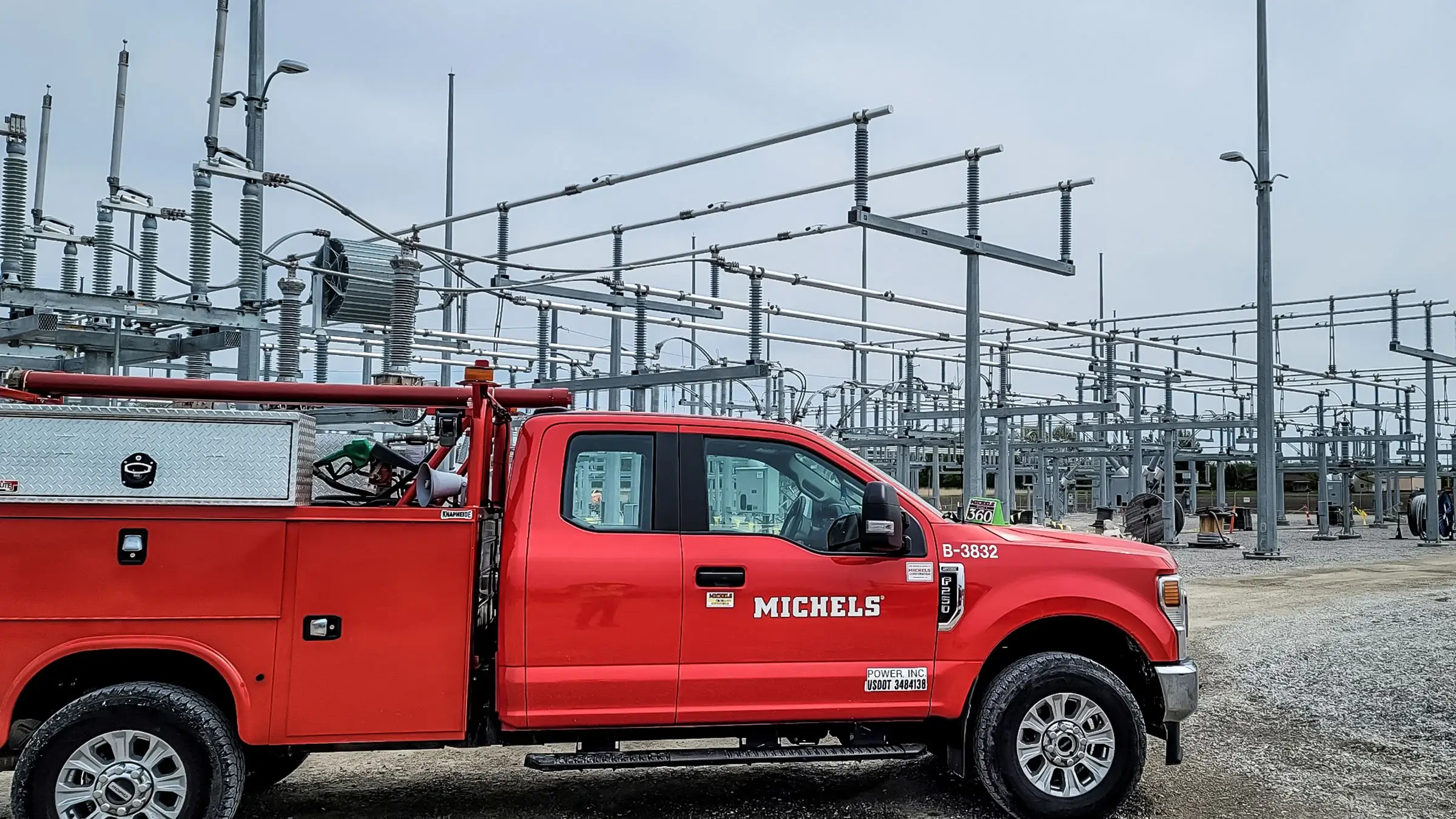 A red Michels pickup truck parked near a substation.