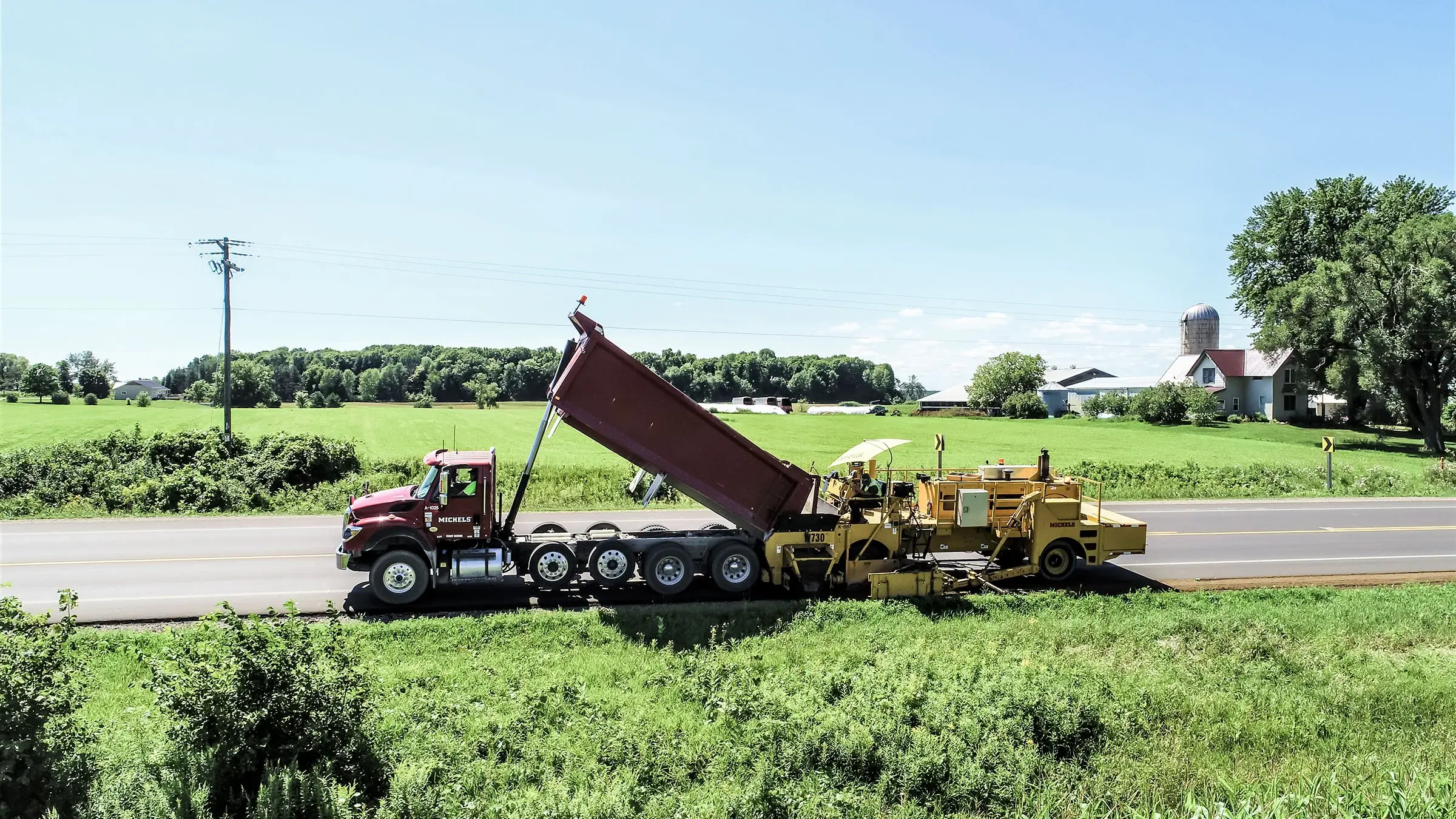 Dump truck fills equipment in order to create gravel shoulder on a road.