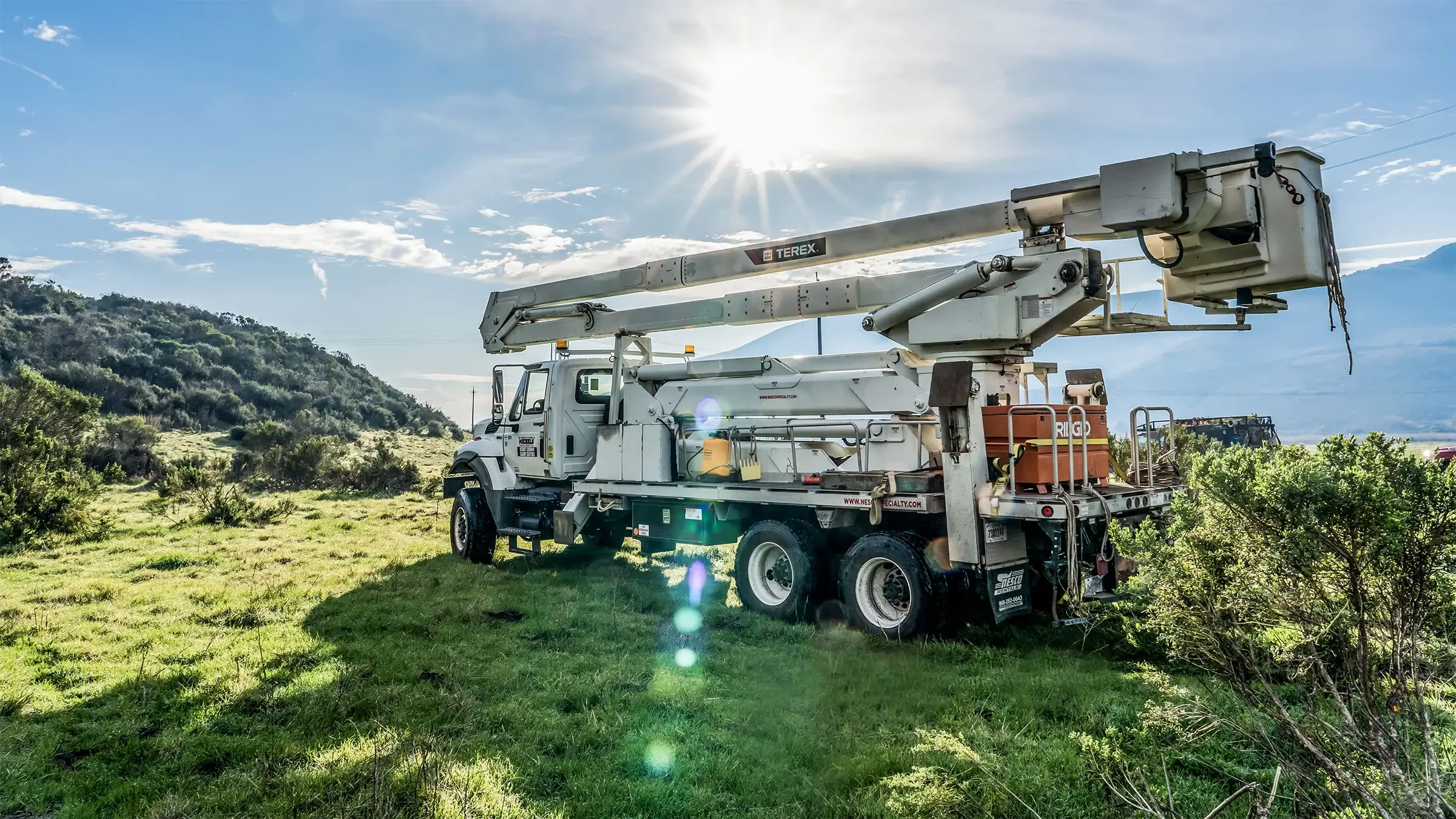 Bucket truck sitting in a grassy field on a sunny day.