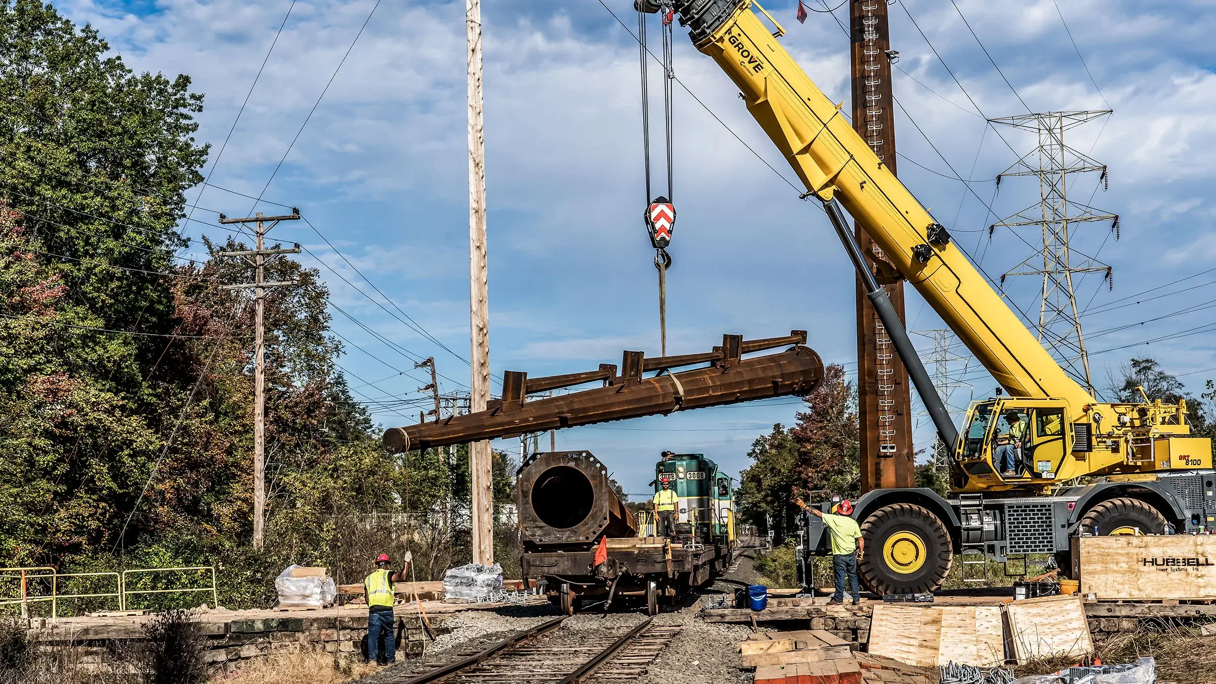 A mobile crane lifts a piece of a power line pole from a rail cart