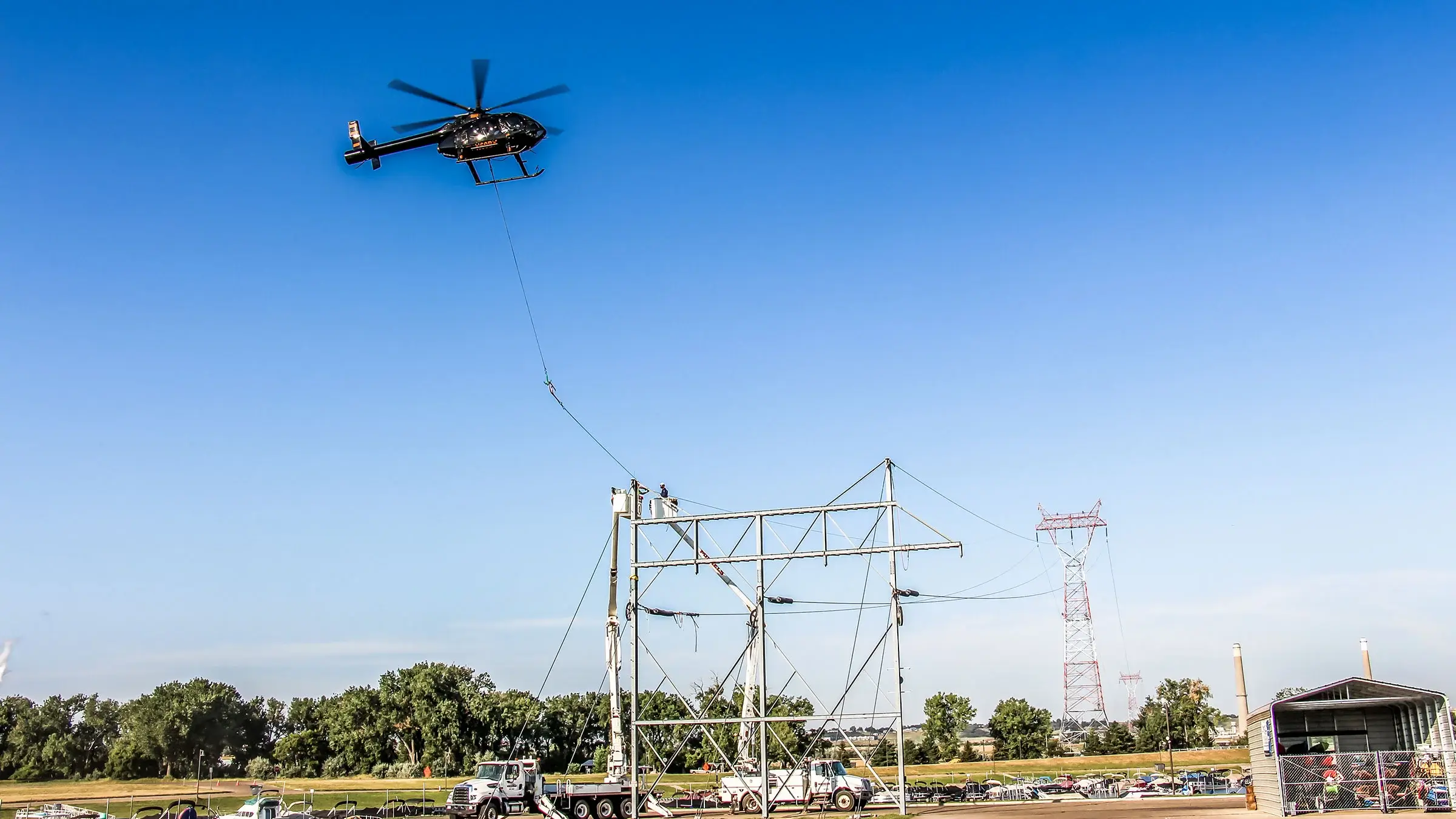 Two bucket trucks and a helicopter operate on large power lines.