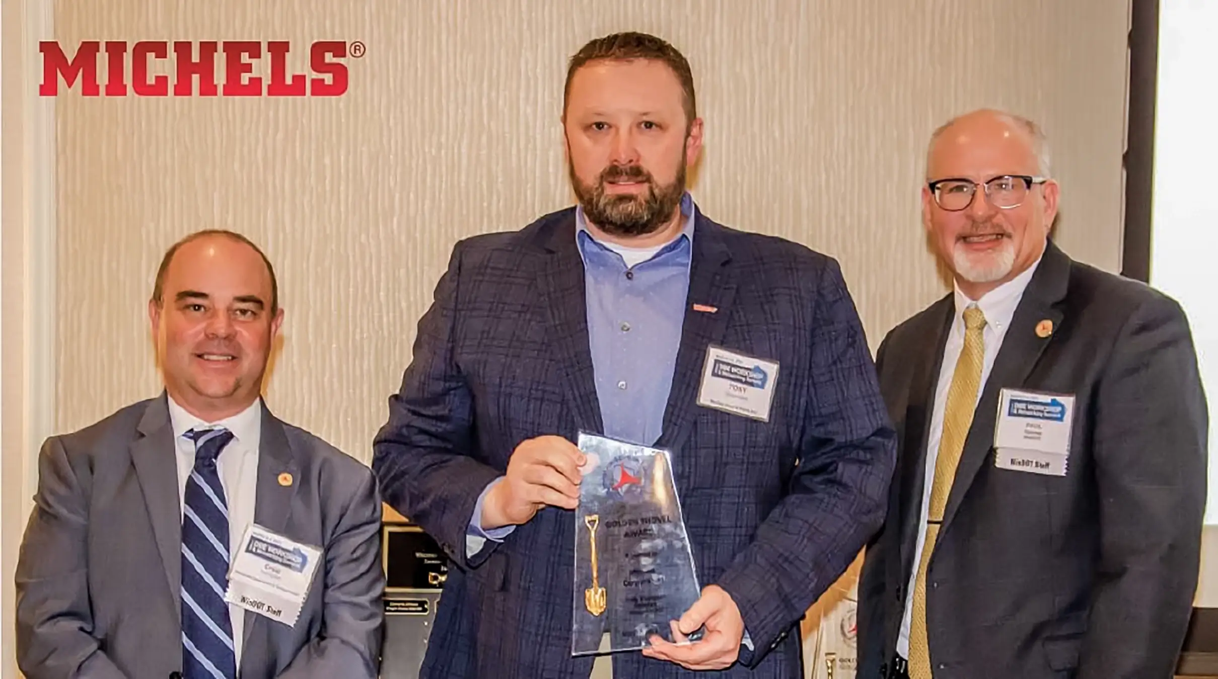 Man with award stands in between two other men