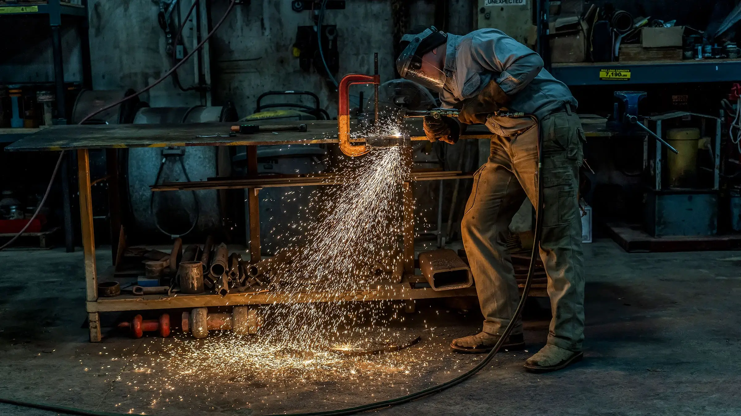 A welder produces a large amount of sparks as he welds a piece of metal at a work bench