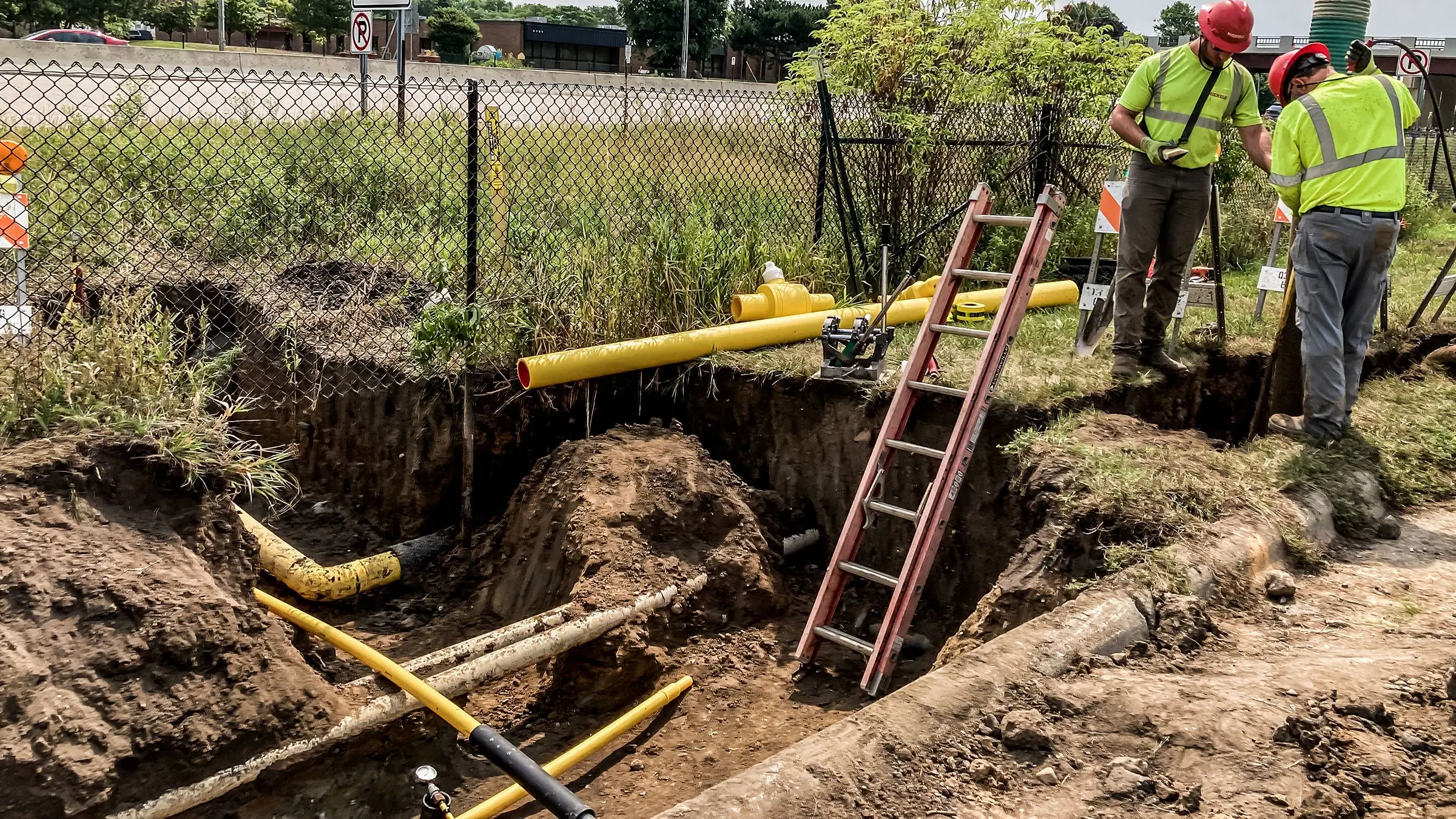 A Michels Utility Services crew operates near a busy highway and small trench