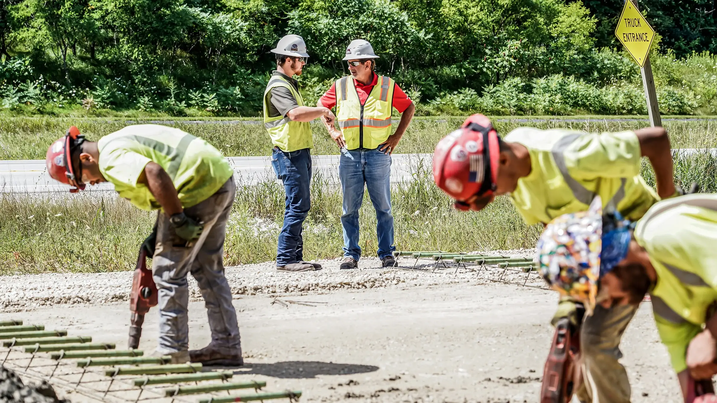 Two Michels crew members chat at a road paving job while it is being worked on by other crew members