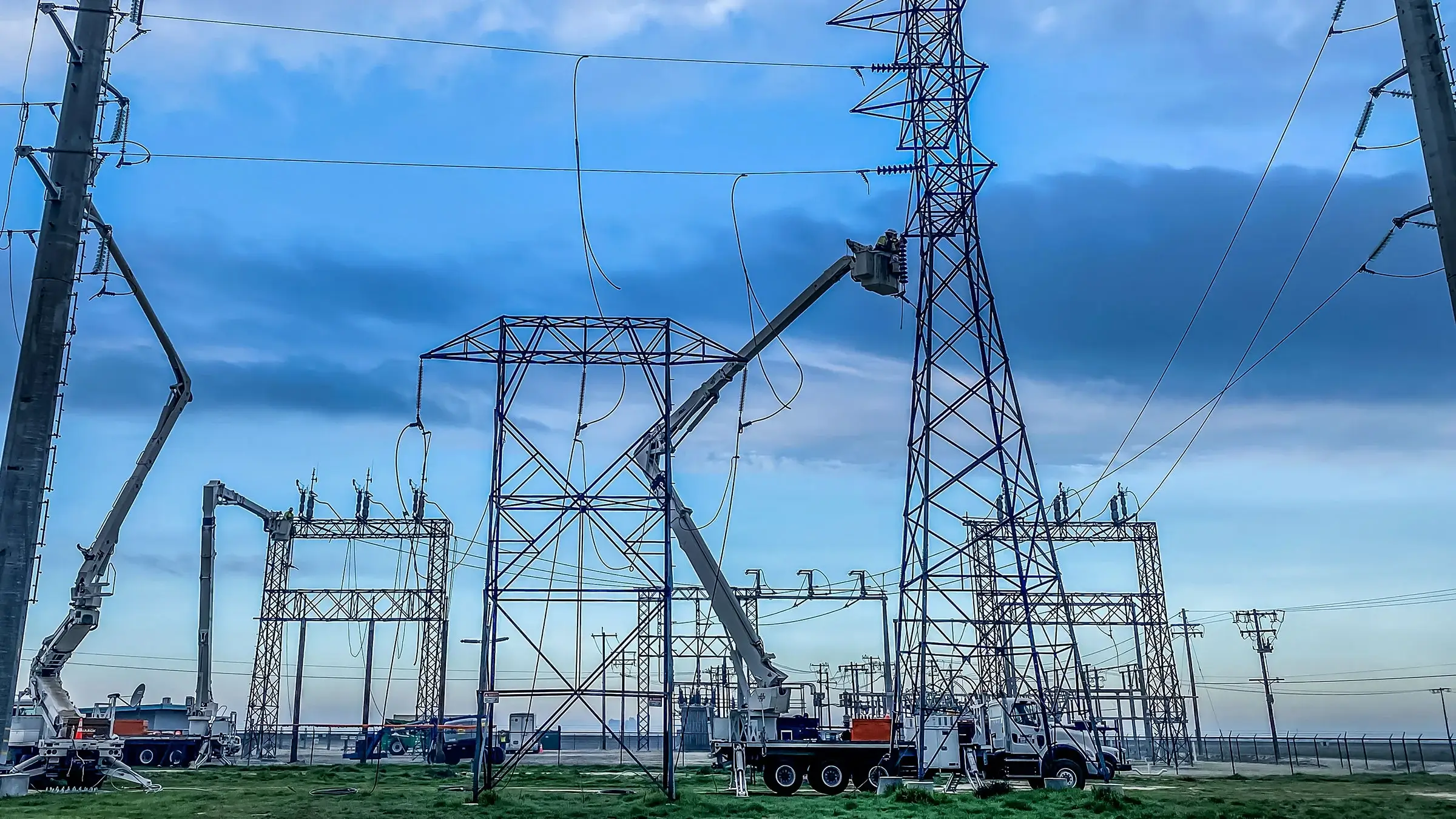 Several bucket trucks operate in an area with many power lines and structures