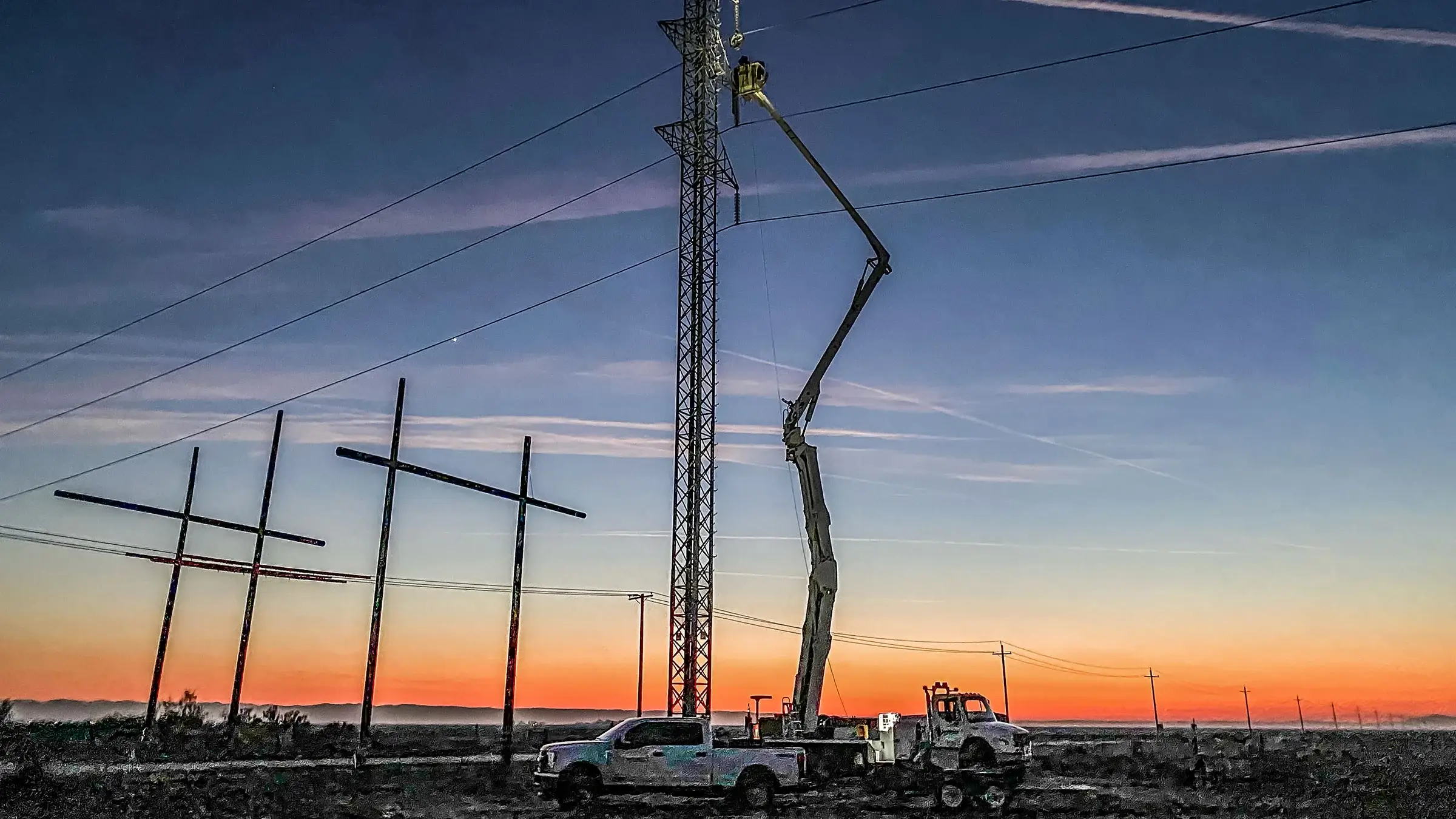 A bucket truck operates at dusk near a power structure