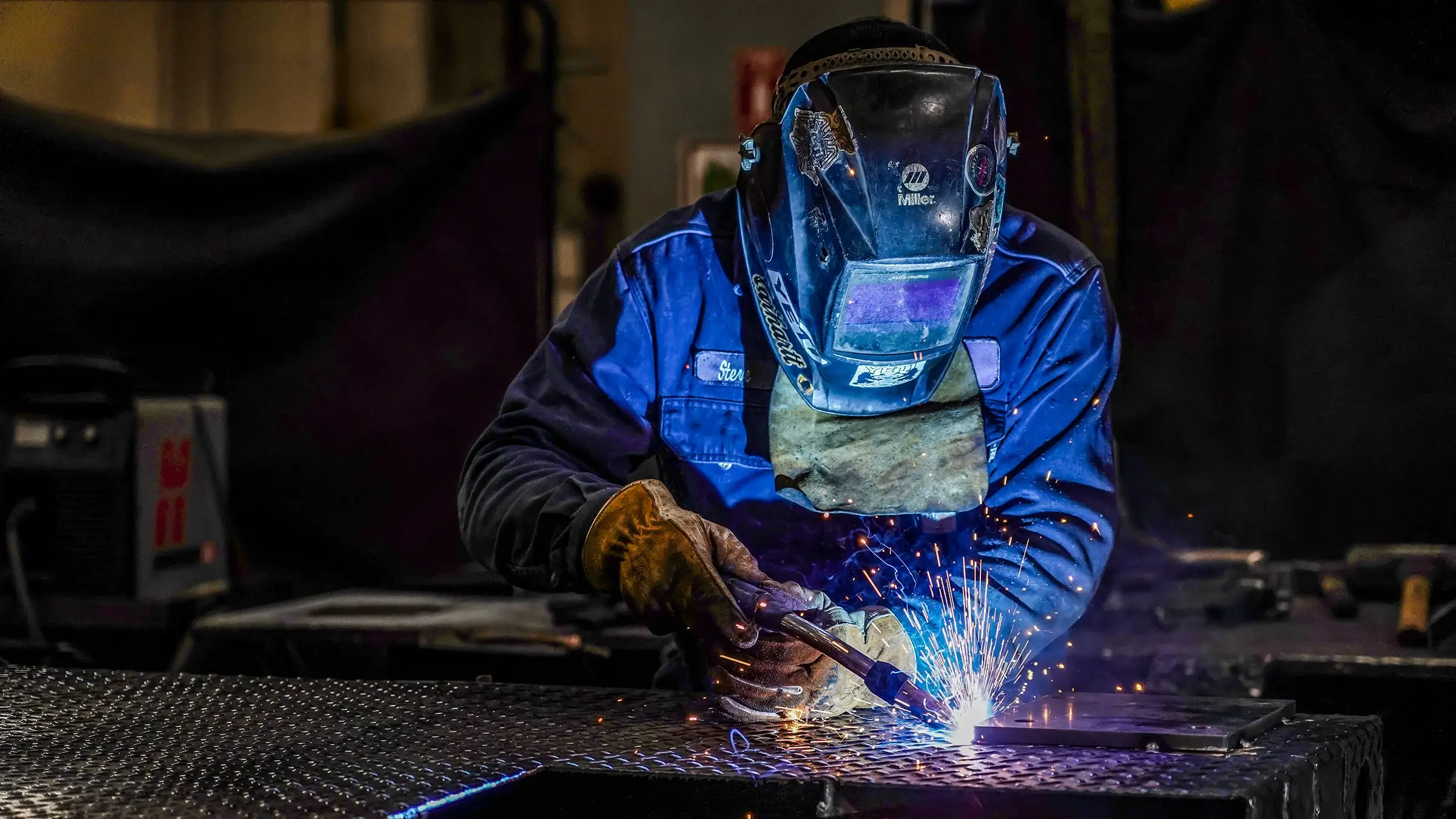A welder produces sparks as they weld a piece of metal