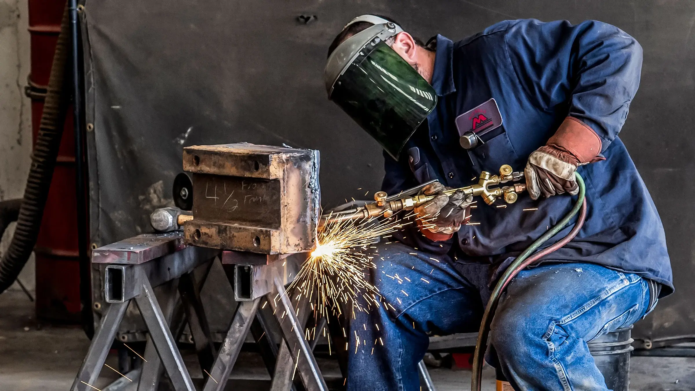 Man welding piece of heavy metal while wearing protective shield