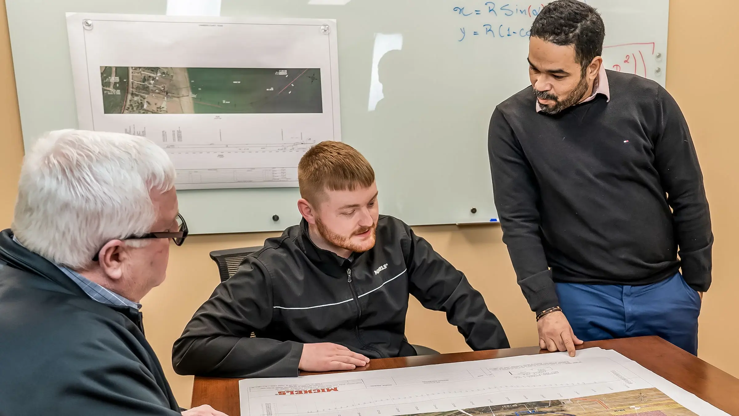 Three people discuss construction plans in a meeting room