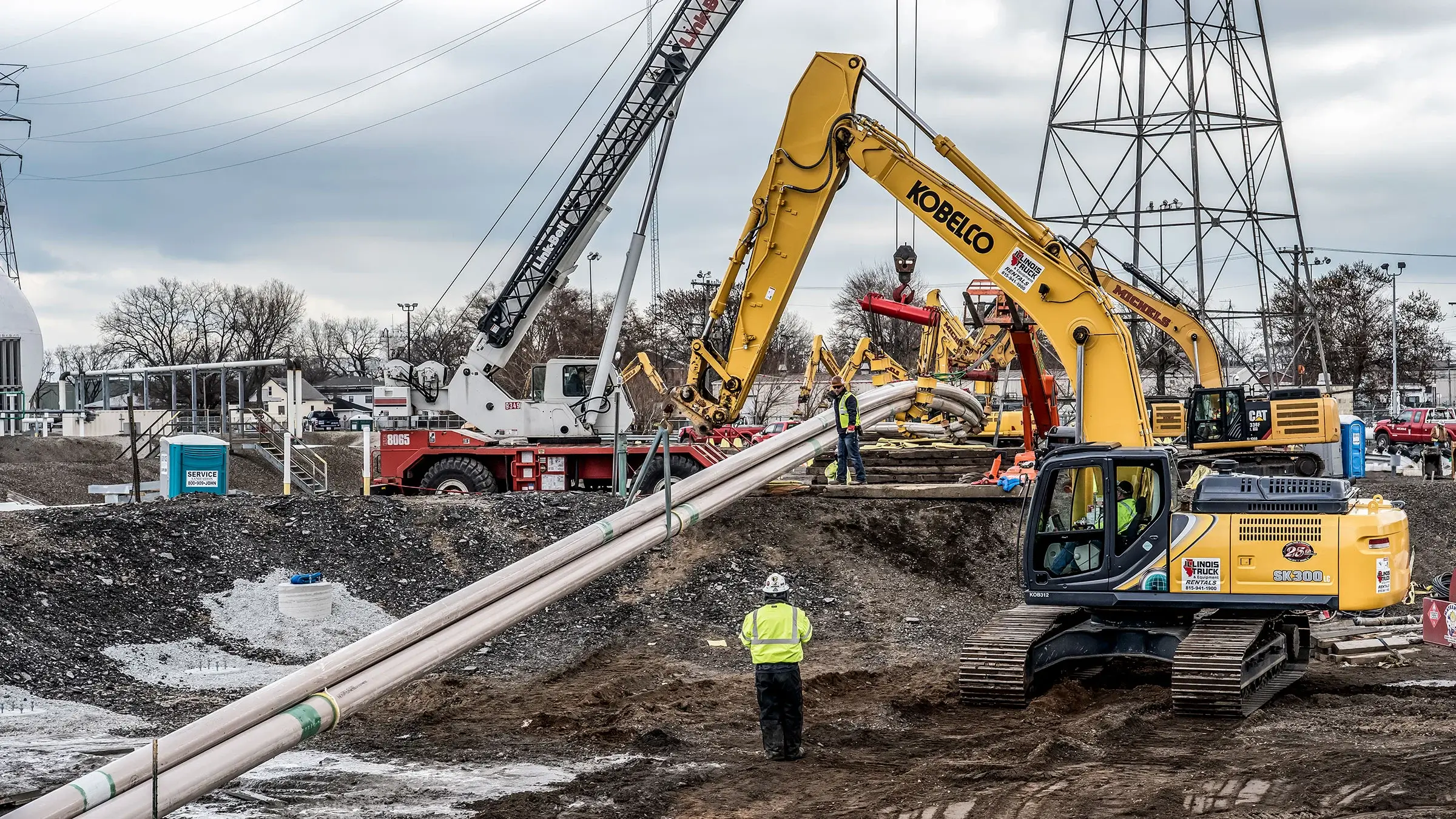 A bundle of pipes being lifted by multiple excavators