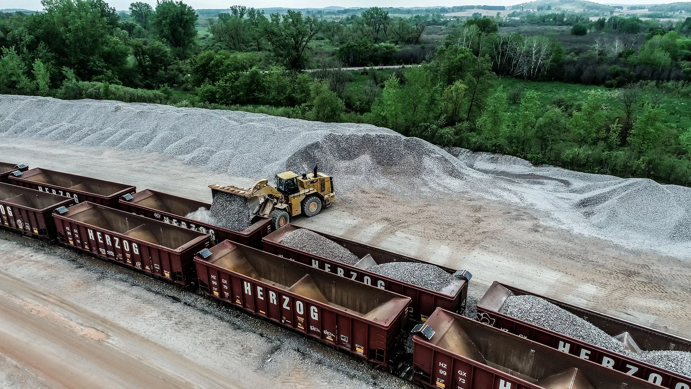 A backhoe unloads ballast stone into rail containers