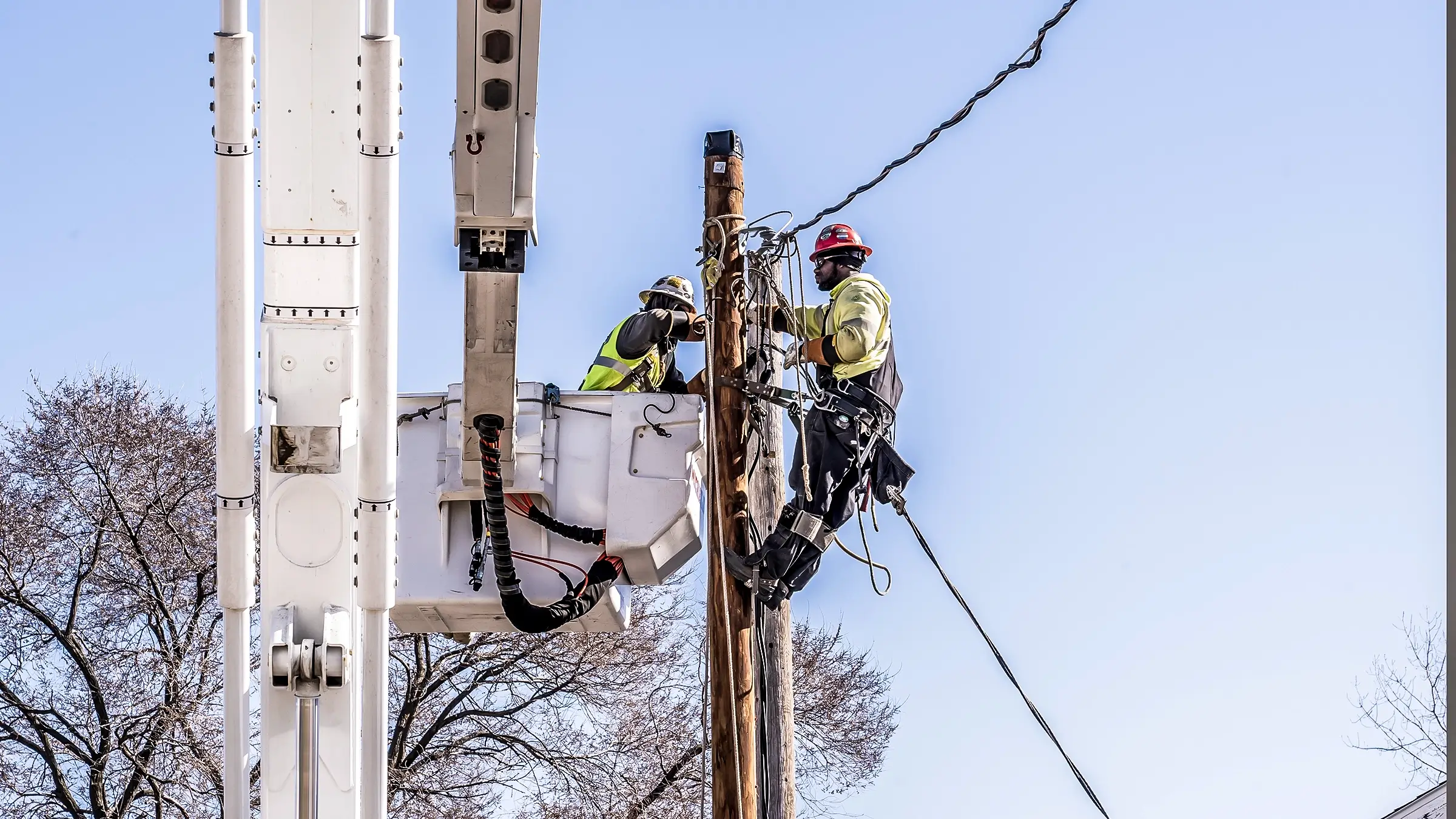 Two line workers operate on a powerline pole.