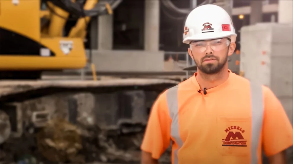 Man wearing hardhat and protective glasses stands on jobsite.