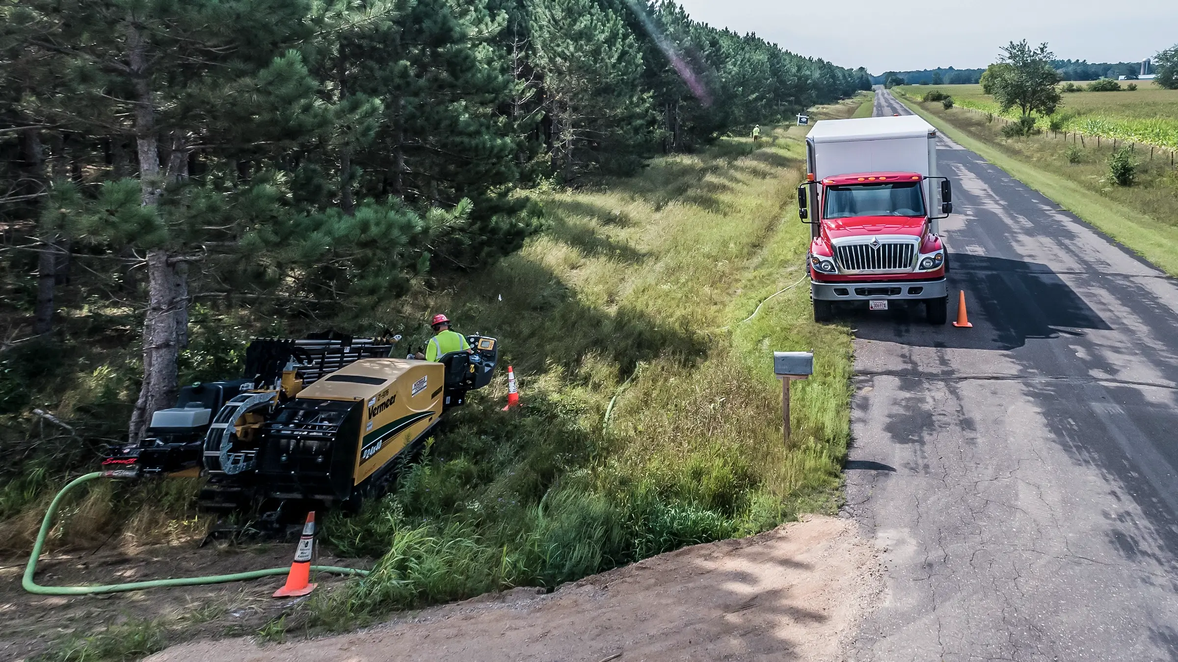 A small HDD rig and box truck work near a rural Wisconsin road.