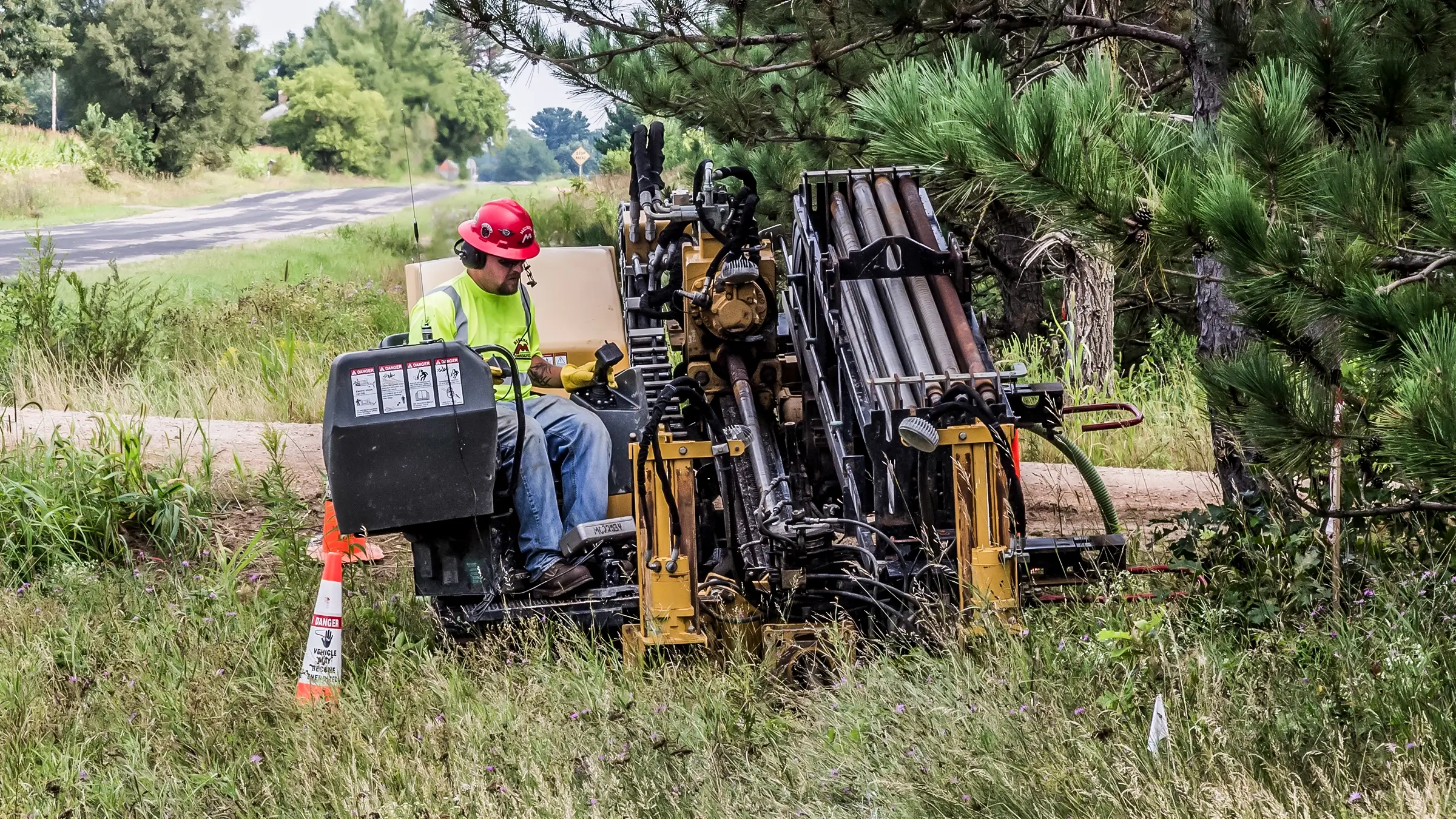 A crew member operates a cable HDD rig near a rural road.