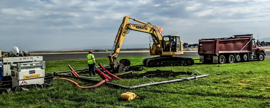 An excavator and crew member work to insert cable into ground near airfield