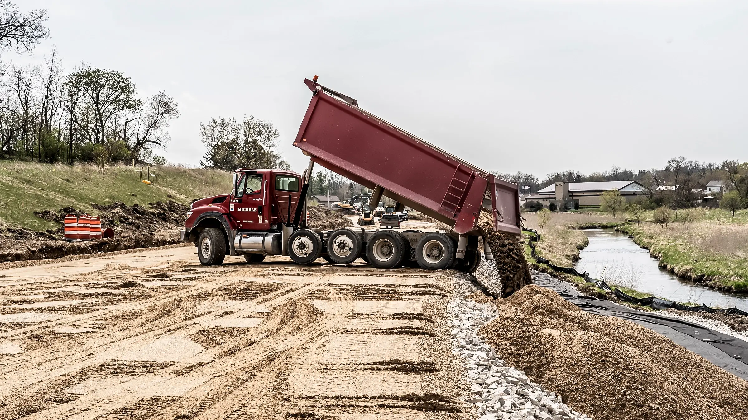 A dump truck places aggregate material near a roadside.