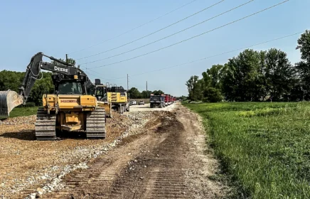 Several excavators and dump trucks operate along a road.