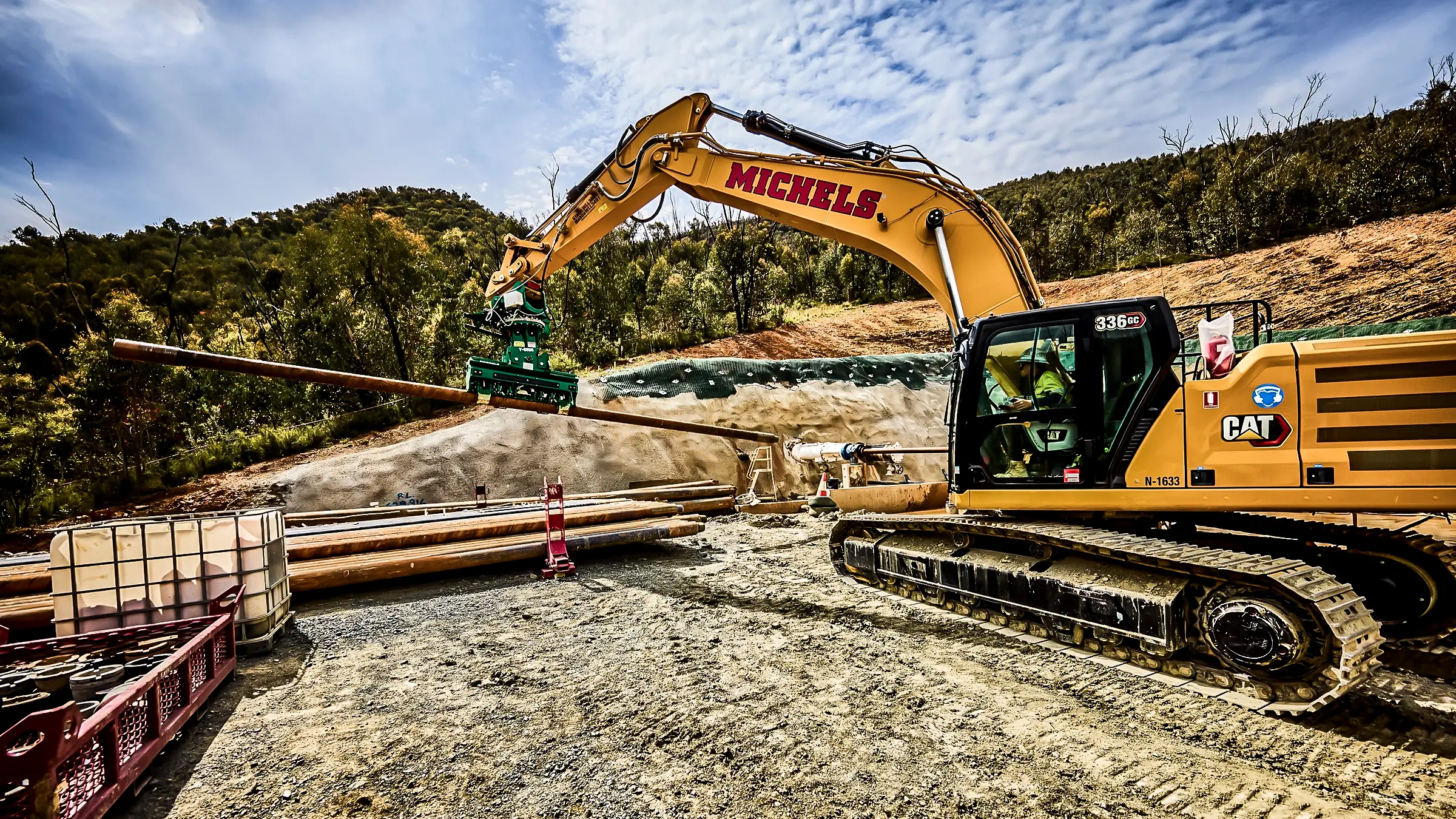 Excavator picking up piece of pipe.