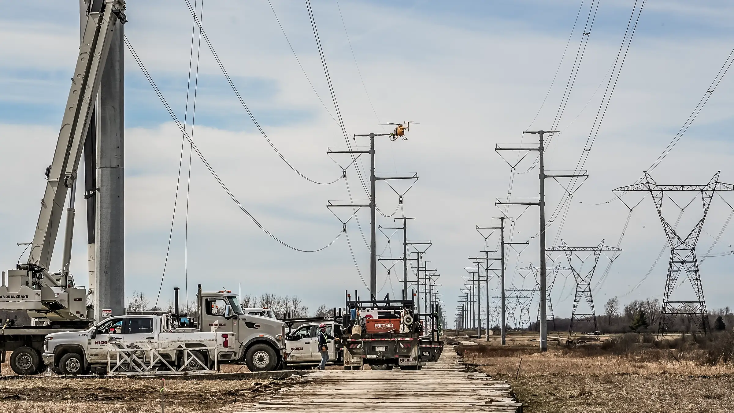 A crane and helicopter operate on large power poles in rural New York.